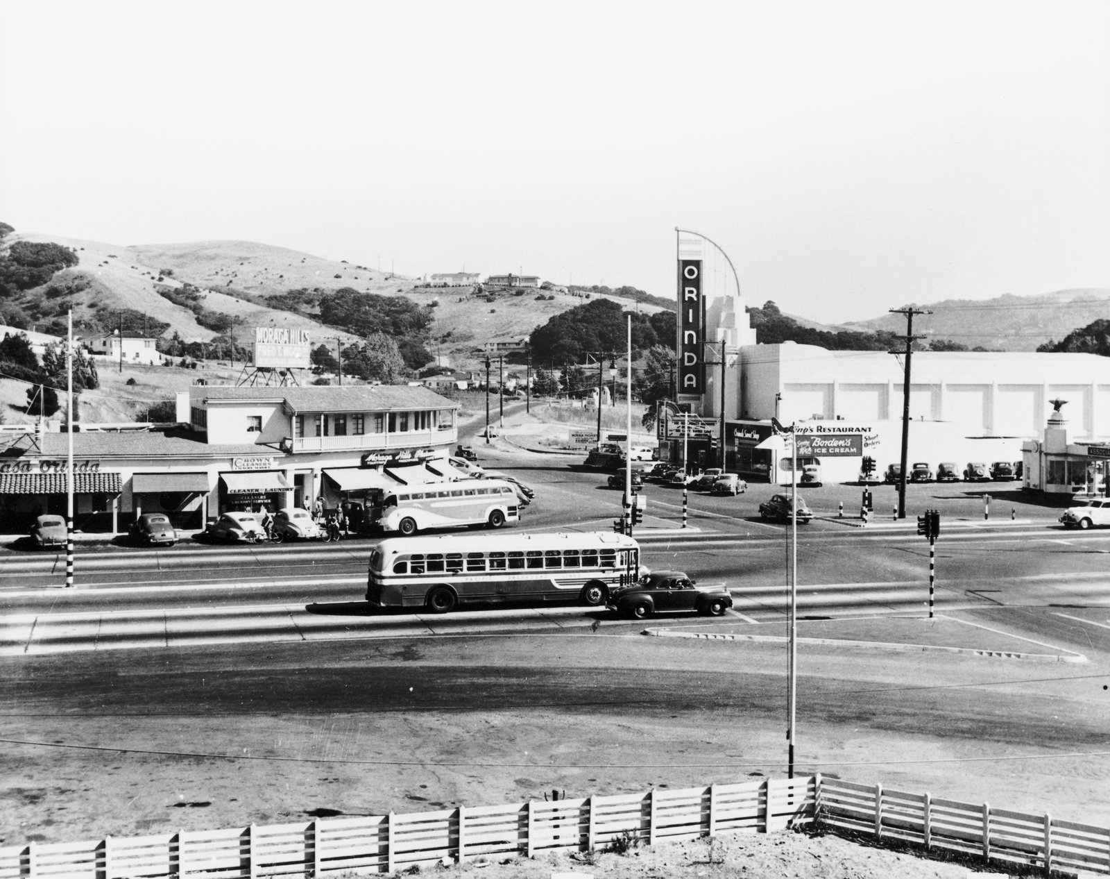 Historic Orinda Crossroads showing the Orinda Theatre sign, local shops, and a bus, with rolling hills in the background